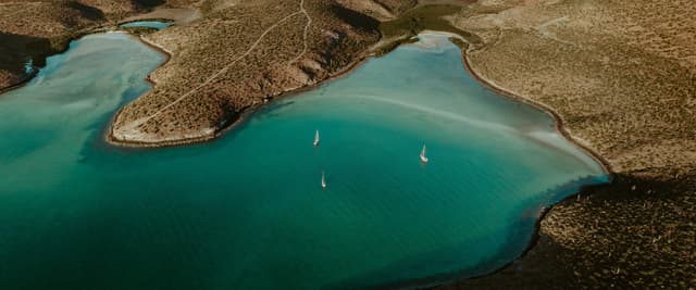 Vista aérea de dos veleros en una tranquila bahía turquesa rodeada de colinas áridas