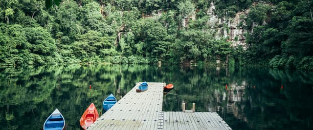 Kayaks de colores en un muelle de un cenote en la selva con aguas verdes y tranquilas