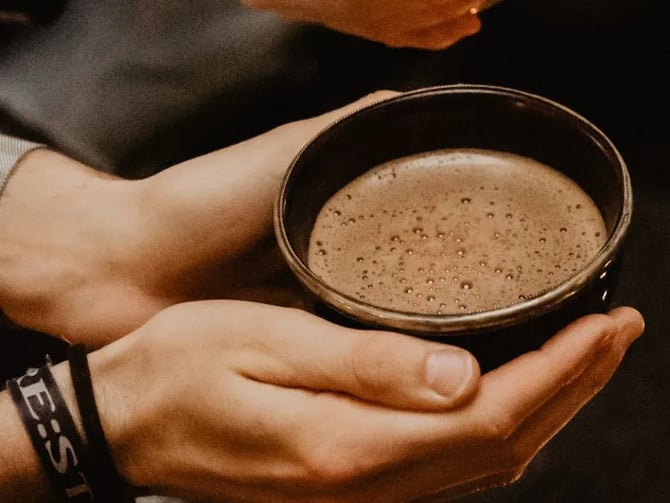 Hands cradling a ceramic bowl of ceremonial cacao drink