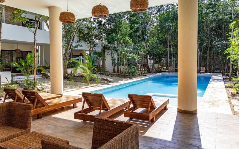 Pool area with lounge chairs, wicker furniture, and decorative hanging lights.