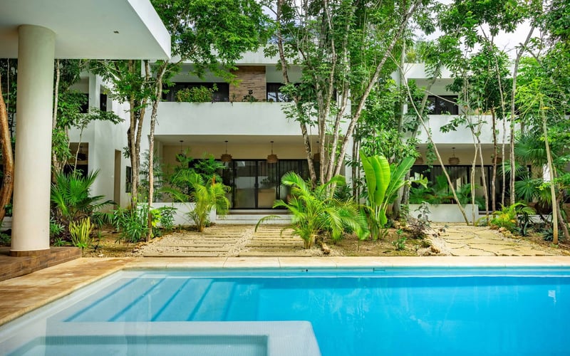 Pool in front of a white building with several trees. Bright blue water and greenery.