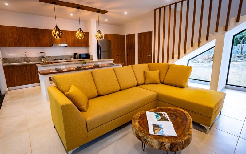 Yellow sectional sofa in modern living room with kitchen and stairs.