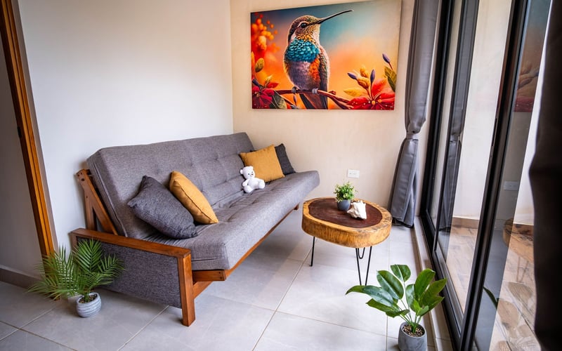 Small living space with gray futon, wood coffee table, and hummingbird art.